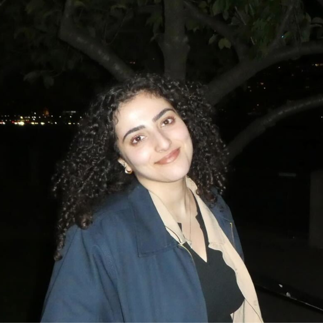 Marwa, a young woman with curly dark brown hair and brown eyes, smiling.