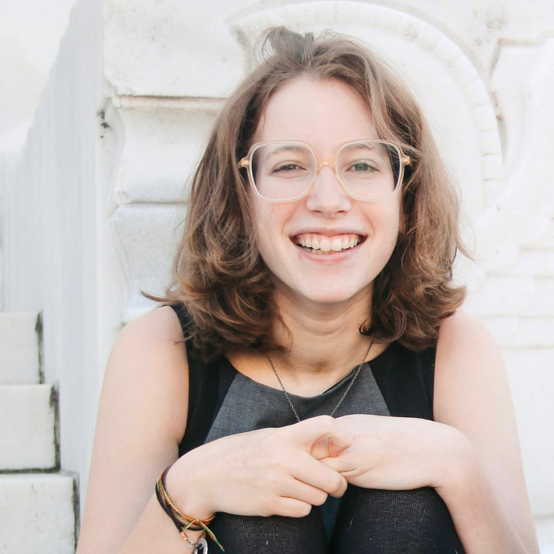 Sarah Day, a young white woman with short brown hair and glasses, smiling at camera. 