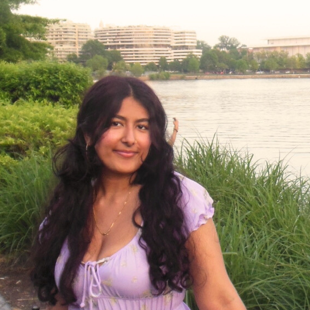 Babisha, a young Asian woman with wavy hair, wearing a purple dress in front of a river.