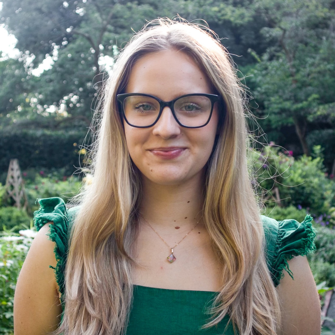 Gianna, a young woman with straight blonde hair, green eyes and black eyeglasses, smiling. 