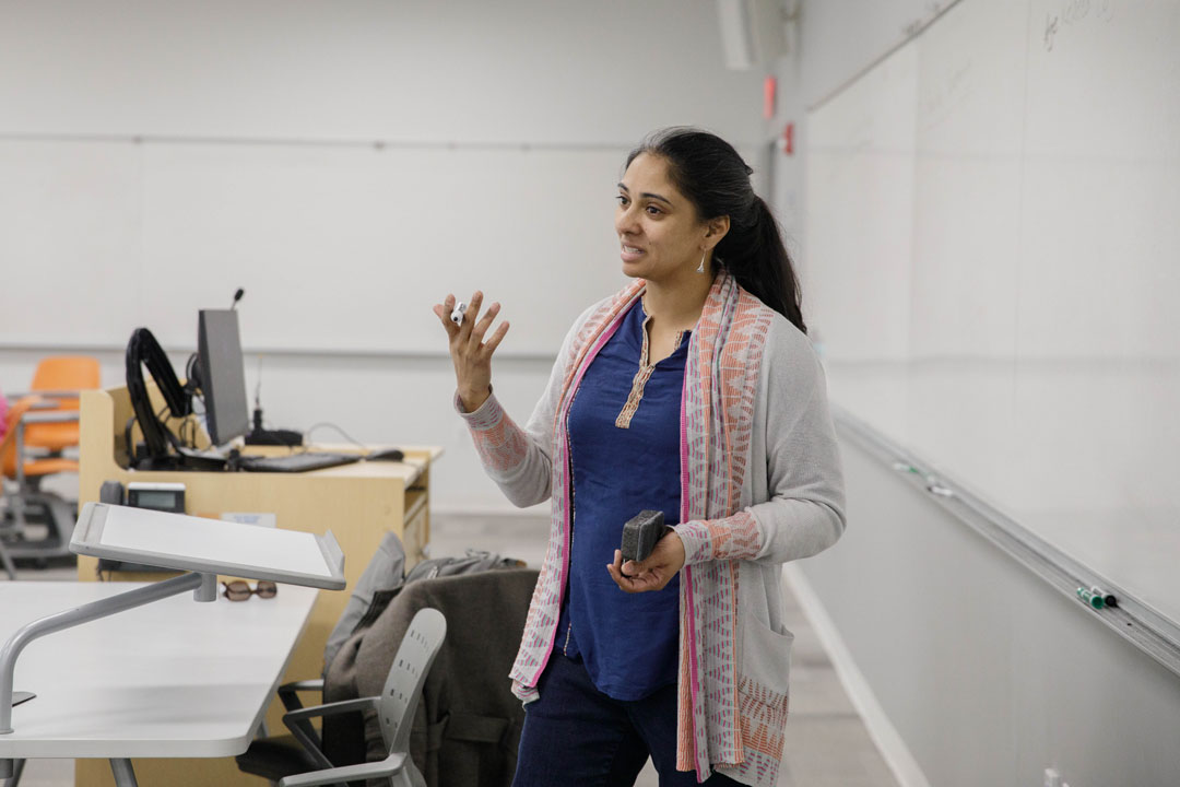 Professor Sangeeta Prasad teaches at the front of a classroom next to a whiteboard