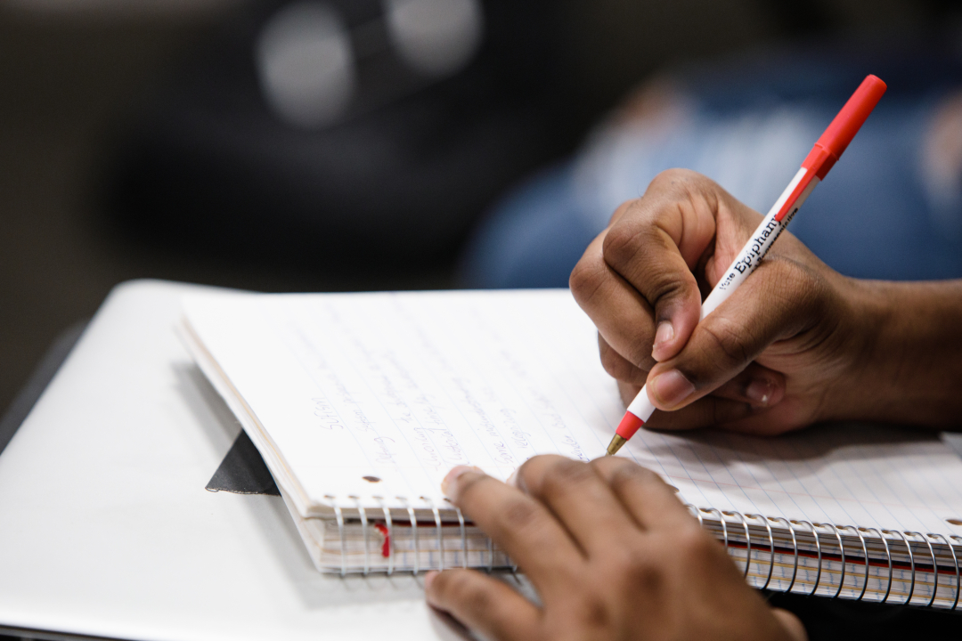 A student's hand writing with a pen on lined notebook paper