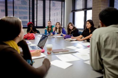 A group of students sitting around a shared table covered with papers and talking